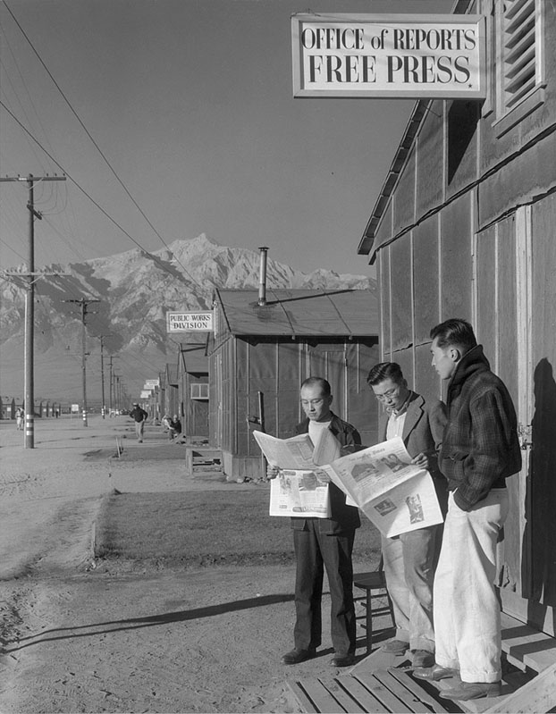 Roy Takeno (far left), with Yuichi Hirata and Nabou Samamura, read the Los Angeles Times in the Manzanar Relocation Camp in California in 1943. Photograph by Ansel Adams.